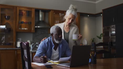 mixed race senior couple using laptop discussing and calculating finances at home
