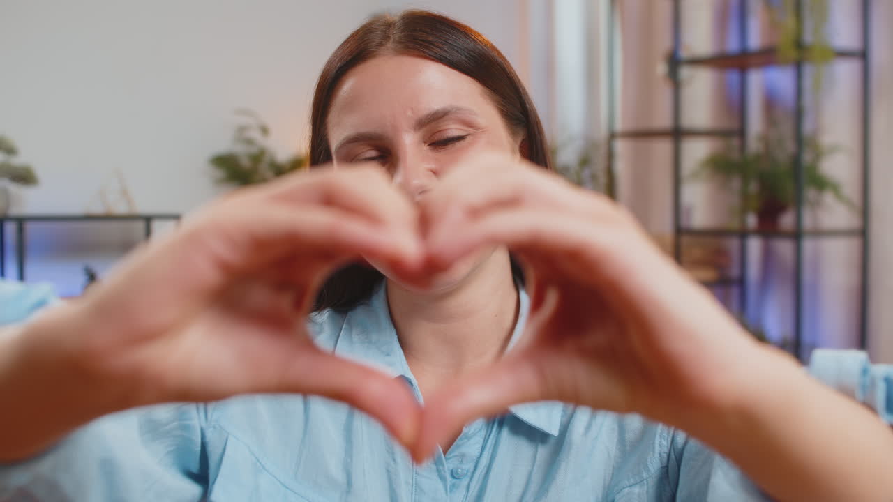 Caucasian young woman makes symbol of love showing heart sign to camera express romantic feelings