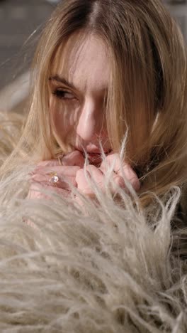 pretty woman with light brown, straight hair wearing a fluffy, light-colored garment outdoors, with their hands adorned with a gold ring and a gemstone on fingers