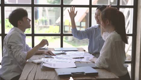 happy successful asian business team give high five sit at table, motivate diverse executives group engaged in team building.