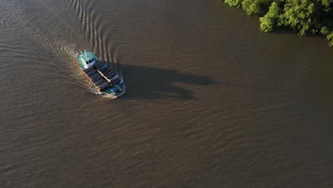 aerial top down showing old cargo ship transporting wood trunks on amazon river during sunlight