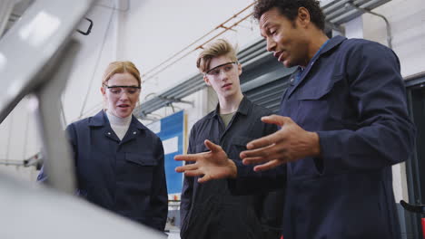 tuteur masculin avec des étudiants regardant le moteur de voiture sur un cours d'apprentissage de mécanicien automobile à l'université