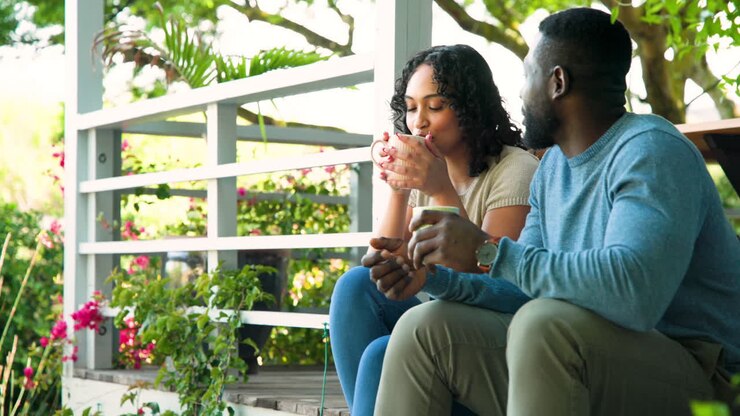 Coppia afroamericana che si rilassa in veranda, godendosi un caffè e una conversazione all'aperto.