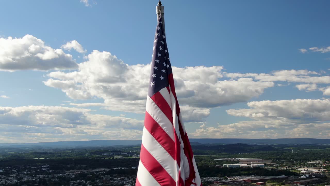 antena de primer plano de la bandera estadounidense, orgullo de los estados unidos, viejas olas de gloria en el viento en un día soleado de verano, centro urbano de la ciudad en el valle de abajo en la distancia, la retirada revela un amplio panorama