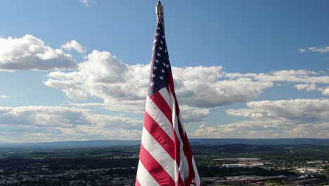 american flag close-up aerial, usa pride, old glory waves in wind on sunny summer day, urban city town center in valley below in distance, pulll-back reveals wide panorama