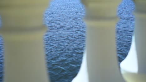 Calm-blue-ocean-waves-moving-between-decorative-white-marble-balcony-pillars