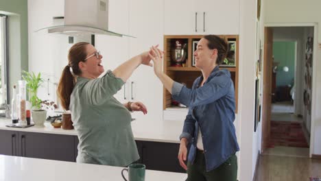 pareja de lesbianas caucásicas sonriendo y bailando en la cocina