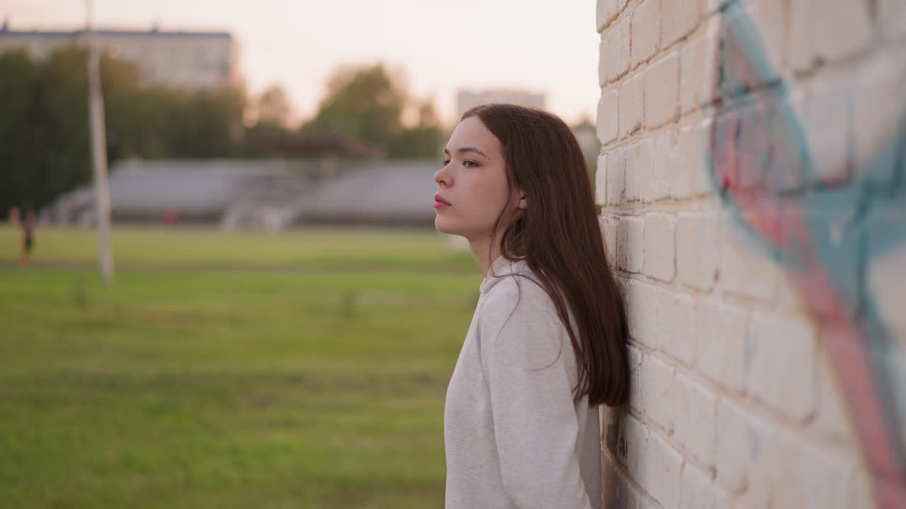 mujer triste se apoya en la pared con graffiti. mujer deprimida se encuentra cerca del estadio sola pensando en los errores pasados en la vida. pasar el tiempo al atardecer