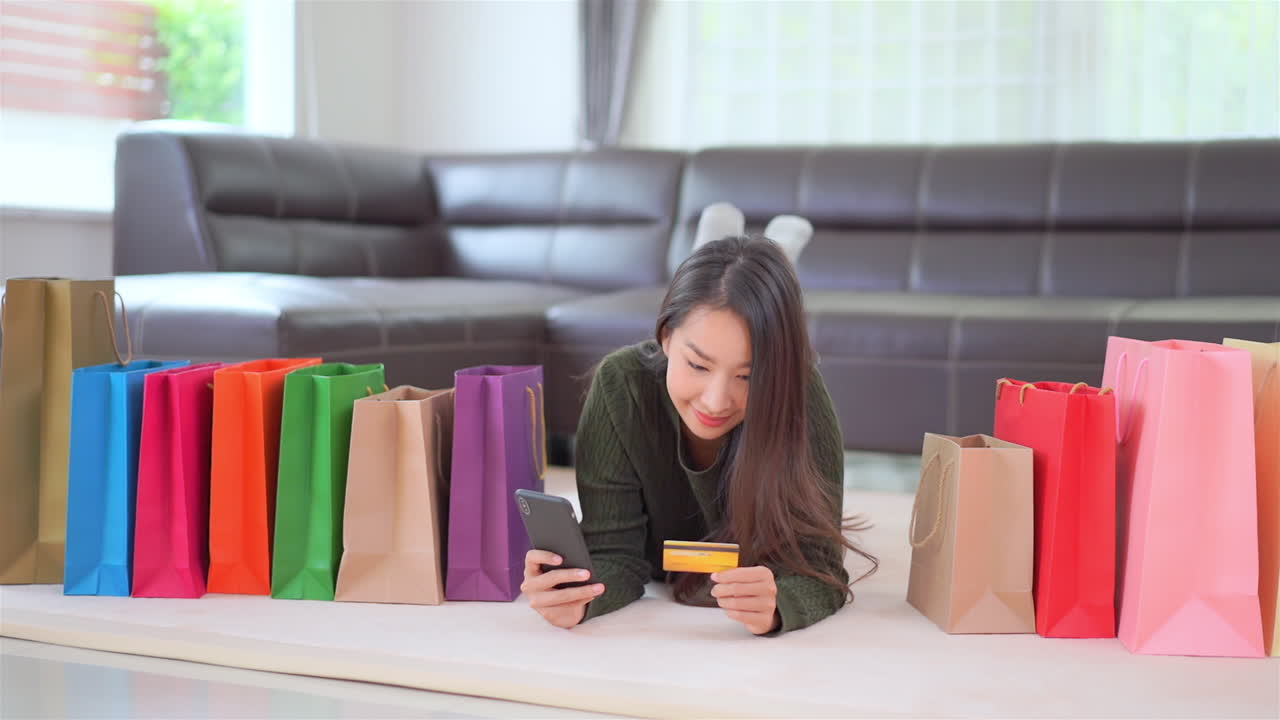 Rich Asian woman surrounded with shopping bags typed in the credit card number to pay online