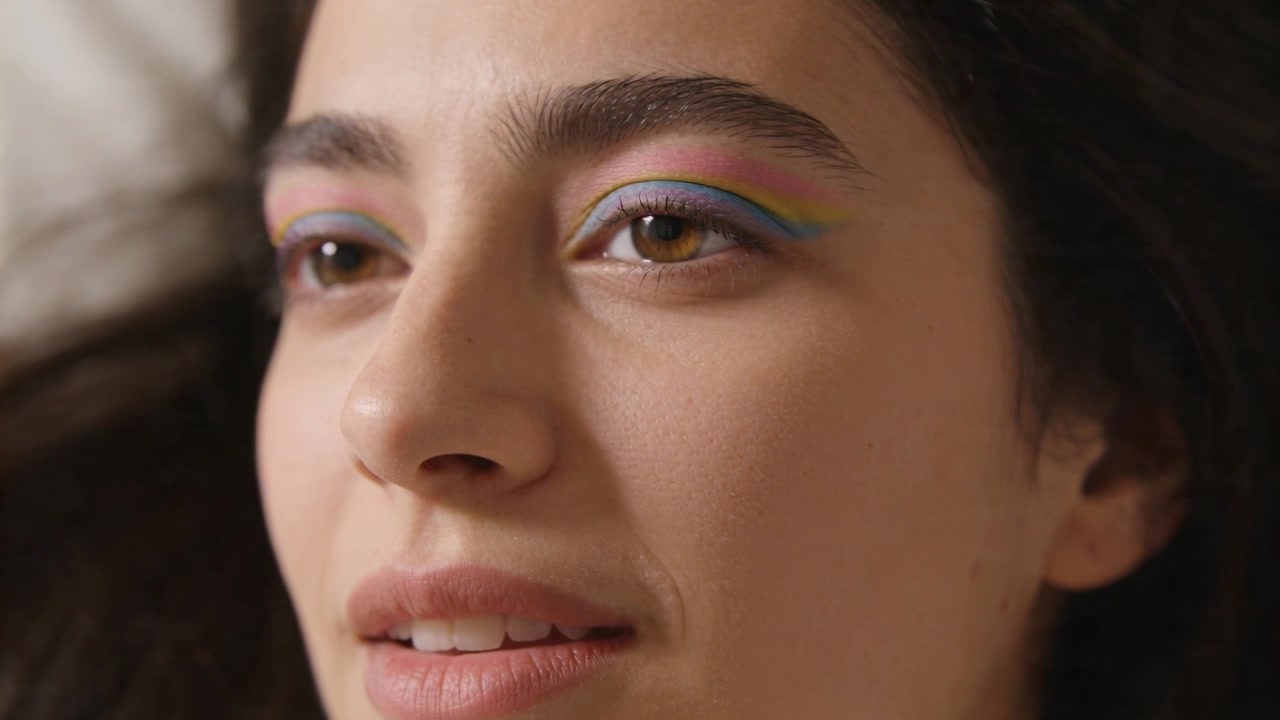 Smiling woman with pastel eyeshadow opening eyes as breathing while lying on bedding for makeup