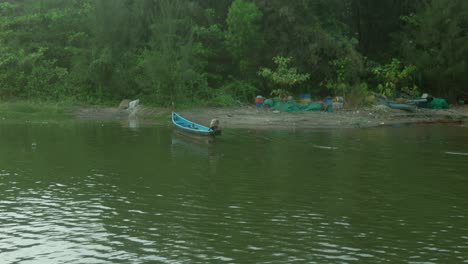 blue boat on the river bank with green trees in the background and a dog passing by