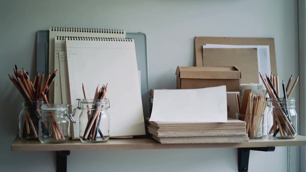 Drifting blank sheet rotating from window gust, landing on paper stack on wooden shelf with pencils