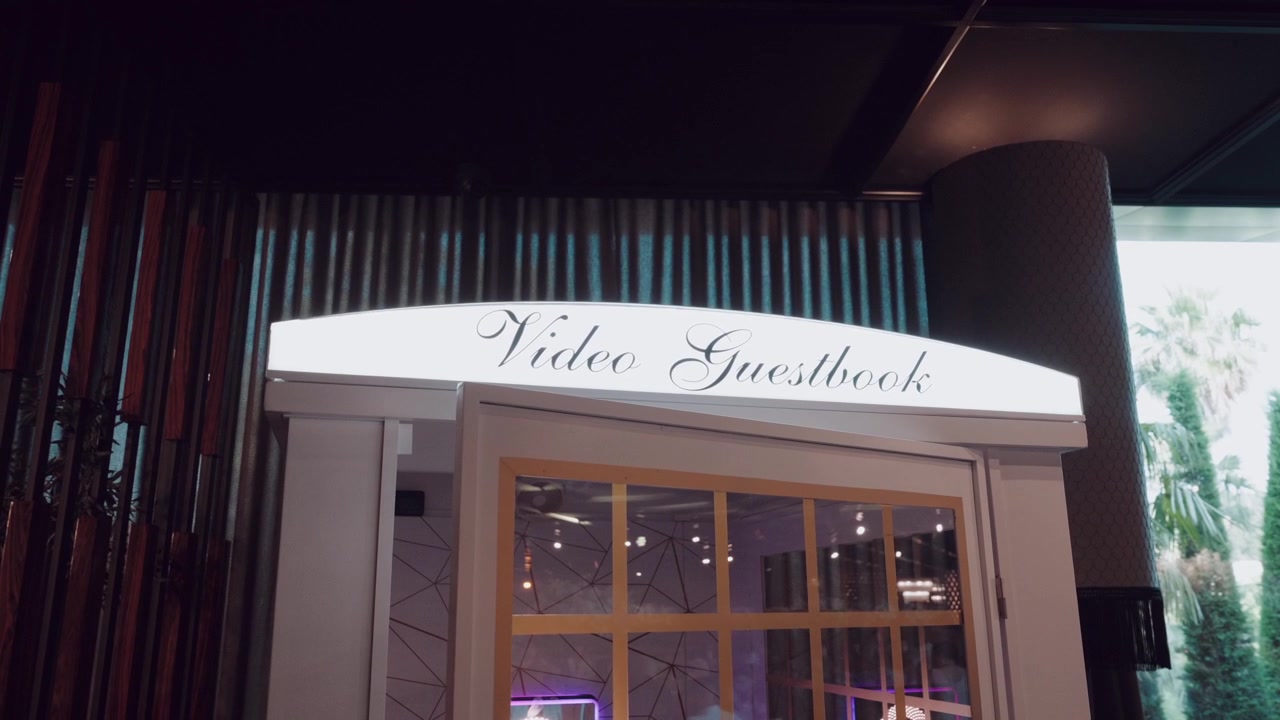 Cabina de videolibro de visitas estilo cabina telefónica blanca con letras caligráficas dentro de un lugar para eventos