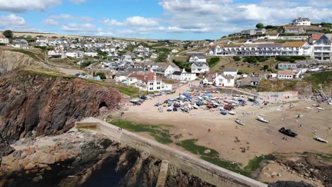 aerial view of boats at hope cove beach at low tide with slow pan left view of rugged coastline cliff