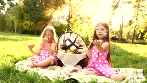 two sisters at picnic blow bubbles.