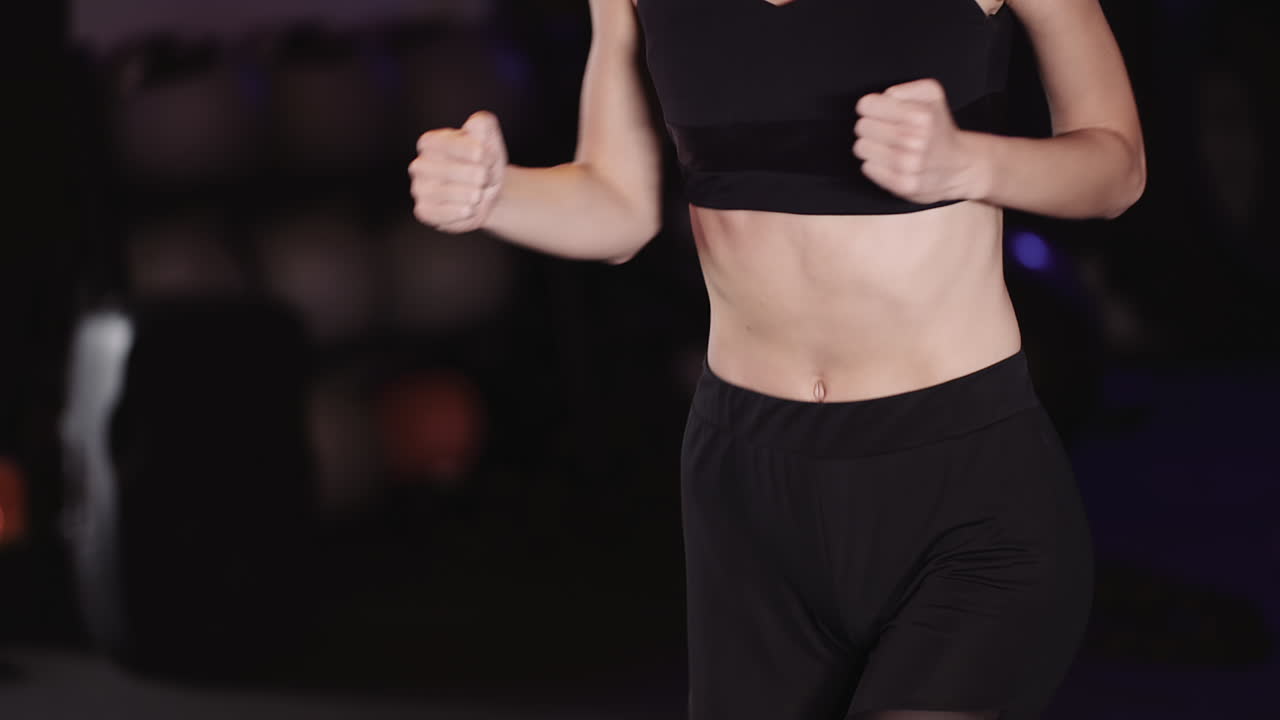 체육관에서 체력 훈련을 하는 동안 제자리에서 조깅하는 날씬한 젊은 여성의 중앙부