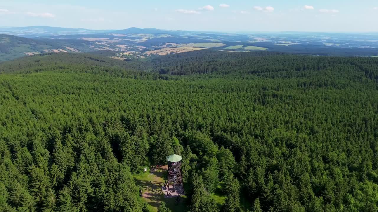 Drone view as it flies over the trees and rotates above the lookout tower on the mountains with the valley in the background