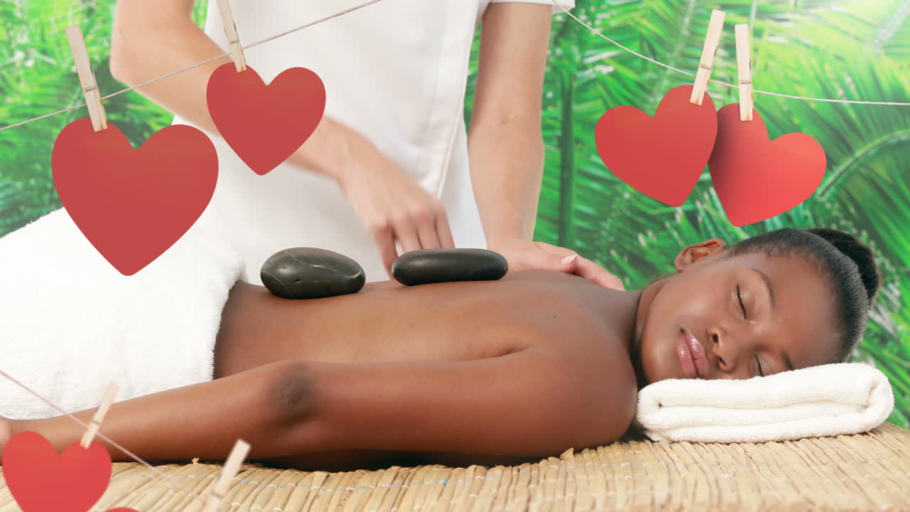 masajista colocando piedras de masaje calientes en la espalda de una mujer negra en el spa para el día de san valentín 4k