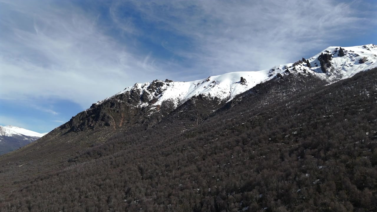 Monte Cerro Catedral parzialmente coperto di neve a Bariloche, Rio Negro, Argentina, durante una giornata di sole con cielo azzurro e nuvole bianche, drone che sorvola al rallentatore