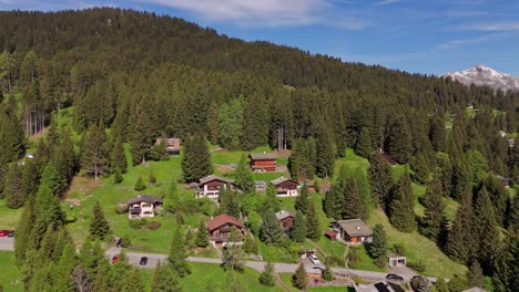 Apartments huts on top of mountain alps in Switzerland. Fir trees on mountain peak. Aerial approaching shot. Vacation Trip in Swiss Alps. Sunny day in summer.