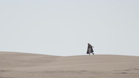 a robed figure struggles across a vast sand dune, then falls to their knees in exhaustion. post-apocalyptic, sci-fi, or fantasy concept of despair, struggle, and survival