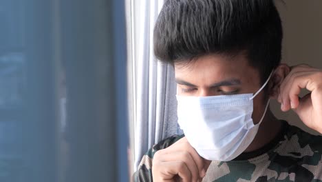 young man wearing a face mask looks out a window