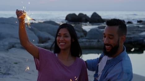 joven pareja feliz de raza mixta divirtiéndose con chispas en la playa 4k