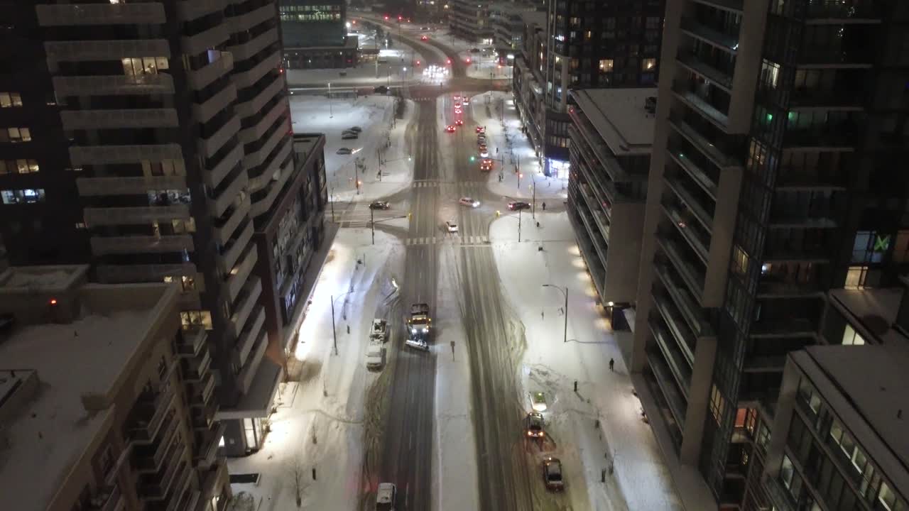 Snowplow truck removing snow from a street at night, between residential buildings in Mississauga, Ontario