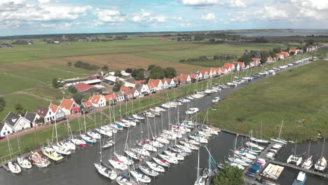 aerial steady and rotation shot following the movement of a sailboat in the marine port area for pleasure boats with typical houses of the dutch village of durgerdam against a blue sky with clouds