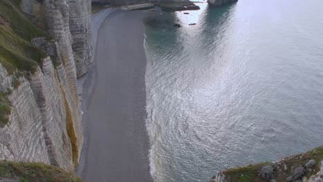 top down shot of empty pebbly etretat beach with calm ocean shore and cliffs