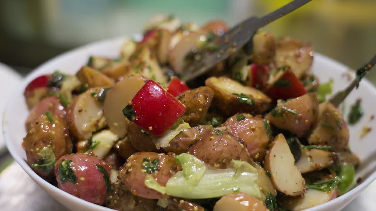 ensalada de patatas recién preparada con patatas rojas, verduras y aderezo mezcladas en un tazón blanco