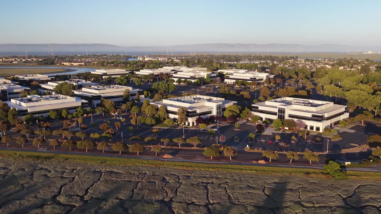Sinar matahari jam emas menerangi gedung perkantoran dan lanskap kawasan bisnis Redwood Shores di Silicon Valley, California, dengan pemandangan rawa garam dan teluk.