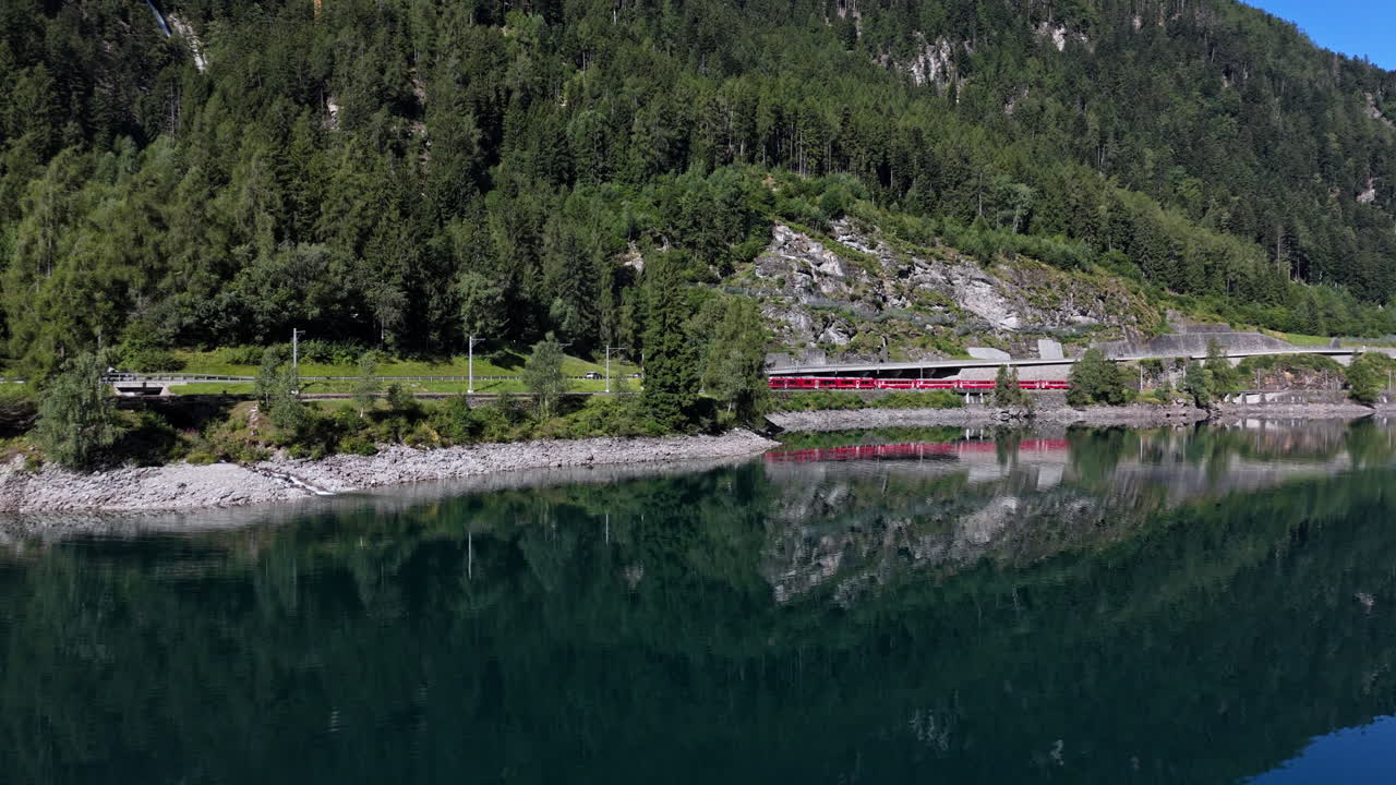 Train travels by scenic lake, mountainous backdrop, serene vibe, blue sky
