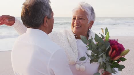 happy hispanic couple embracing and laughing on beach after proposal