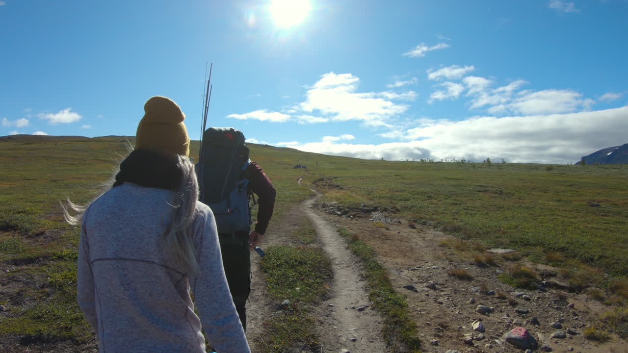 Two people hiking on a dirt path in a vast, sunny natural landscape