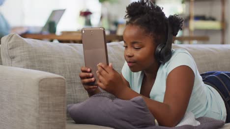 happy african american girl lying on sofa using tablet