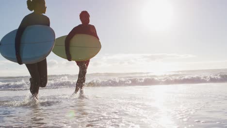 african american couple running with surfboards on the beach