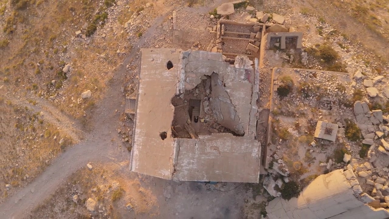 Metraje aéreo de dron mostrando a un piloto de dron dentro de un antiguo edificio de piedra en la montaña, rodeado de terreno accidentado.