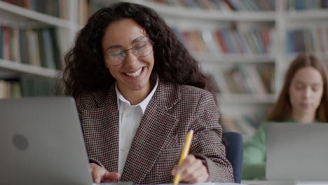 happy woman studying in a library with laptop