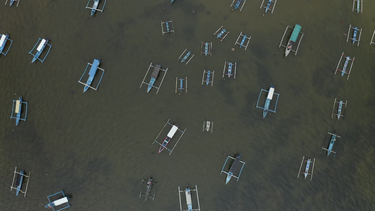 Top down aerial view of traditional outrigger boats anchored in calm shallow water near the coast in Bali creating a peaceful maritime pattern