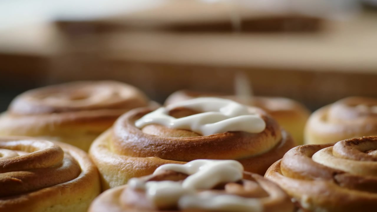 Primo piano di girelle alla cannella glassate con glassa calda alla vaniglia, pasticcere che cola glassa lucida su dorato