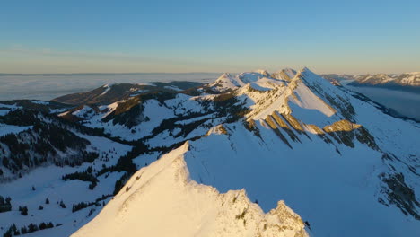 Volando-Sobre-Una-Cresta-Blanca-Como-La-Nieve-De-Las-Hermosas-Cumbres-Alpinas-De-Suiza-En-Una-Impresionante-Puesta-De-Sol-De-Invierno---Toma-Aérea