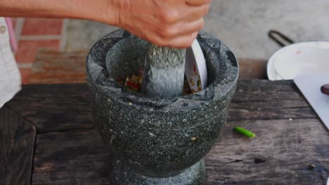 Mano-Femenina-Con-Mortero-De-Piedra-En-Un-Mortero-Golpeando-Ingredientes---Comida-Tailandesa