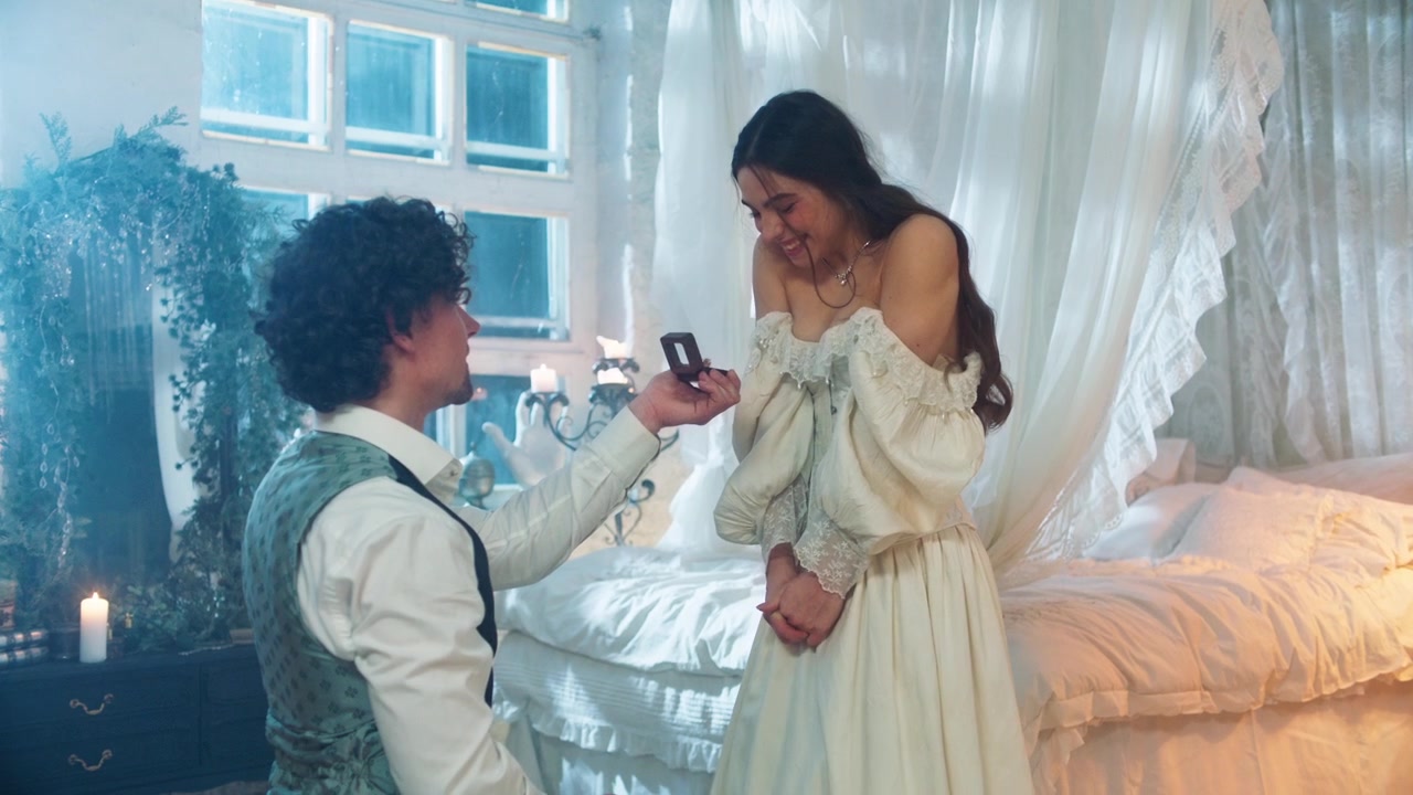 Man Proposes to Woman with Engagement Ring in Romantic Bedroom