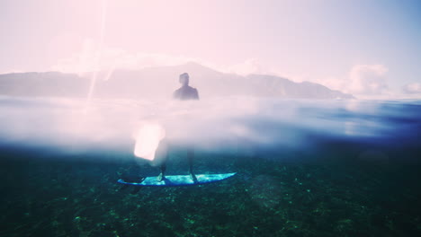 Underwater-view-of-surfer-distorted-as-they-balance-standing-on-short-board-over-reef,-shifting-feet-to-wide-stance