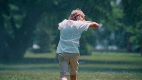 Kleiner-Junge-Läuft-Unter-Sprinkleranlagen-Im-Park-Und-Versteckt-Seine-Ohren-Allein-Vor-Wassertropfen