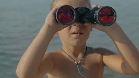 vista en cámara lenta de un niño pequeño observando con binoculares contra el mar borroso