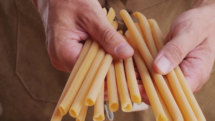 Primo piano di mani che tengono pasta tubolare secca