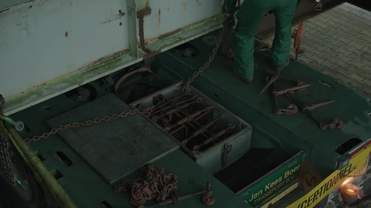 트럭에서 쇠사슬을 집어 들고 대들보를 묶는 남자