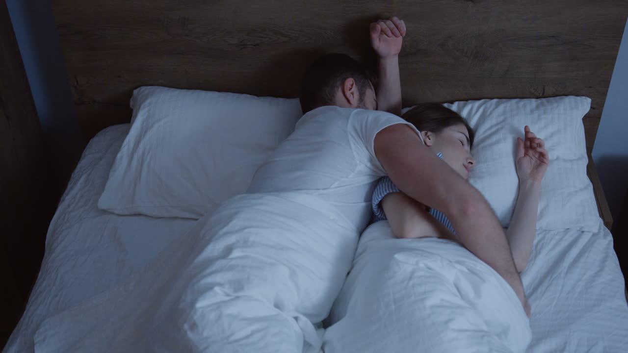 밤에 침대에서 자고있는 젊은 백인 부부